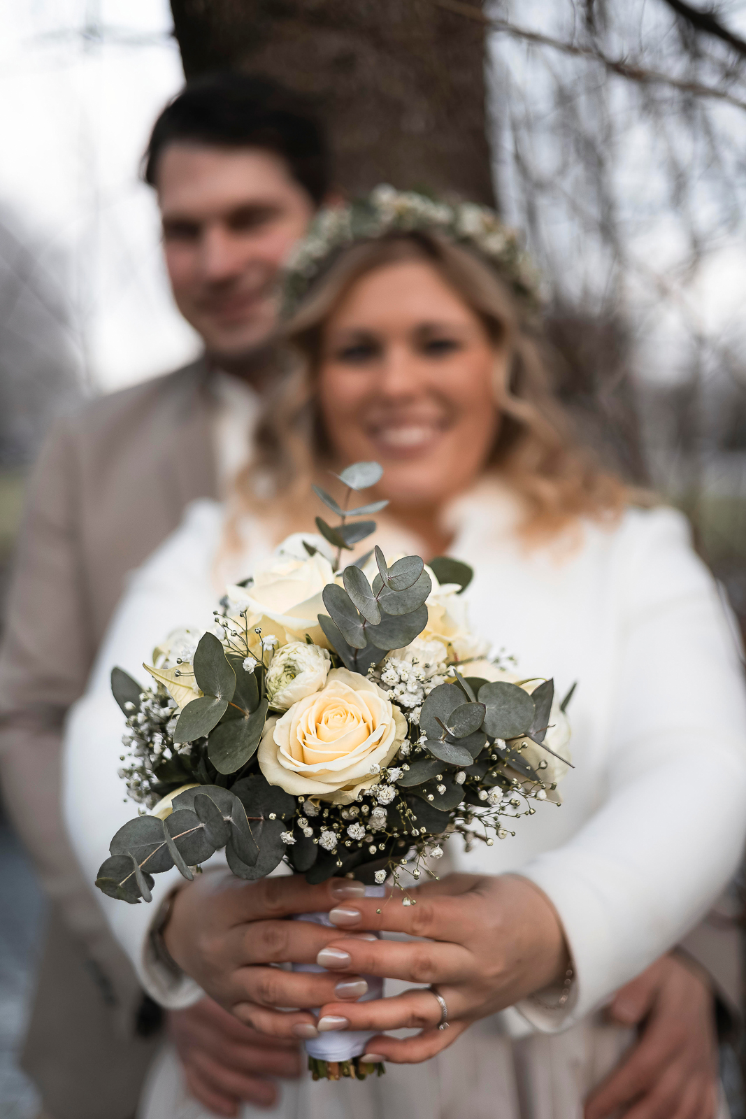 Winterhochzeit Mering - Brautstrauß Detail mit Brautpaar im Hintergrund